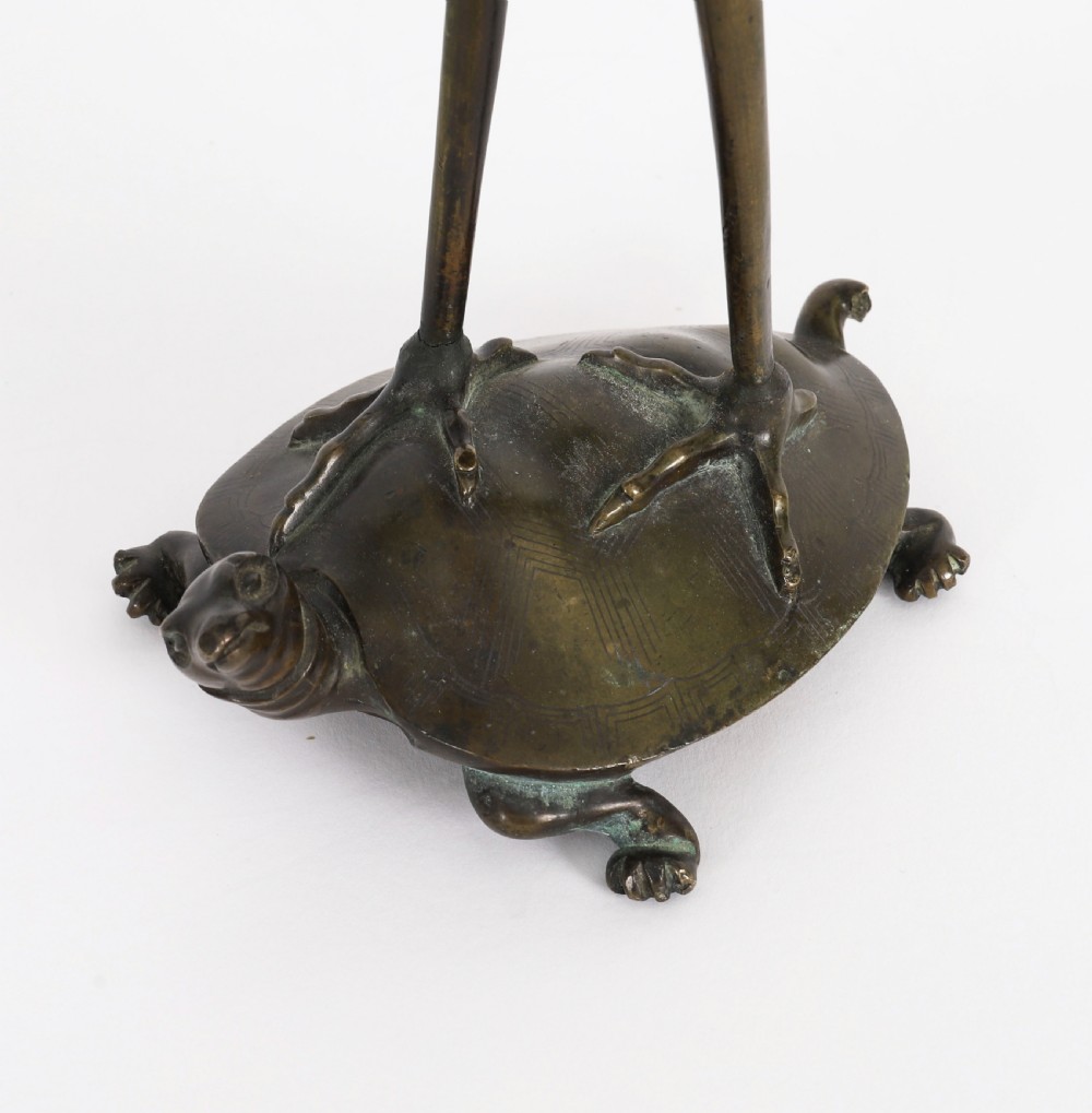 A pair of 19th-century Japanese dark bronze pricket candlesticks formed as cranes standing on tortoises holding lotus stems in their beaks. View X