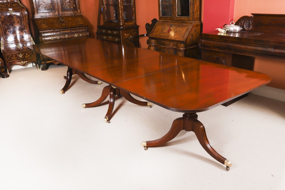 A long polished mahogany triple pillar dining table featuring splayed tripod legs fitted with brass castors.