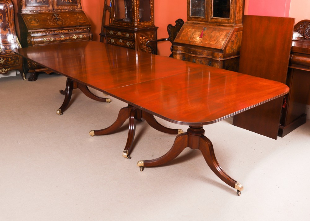 A long polished mahogany triple pillar dining table featuring splayed tripod legs fitted with brass castors. View III