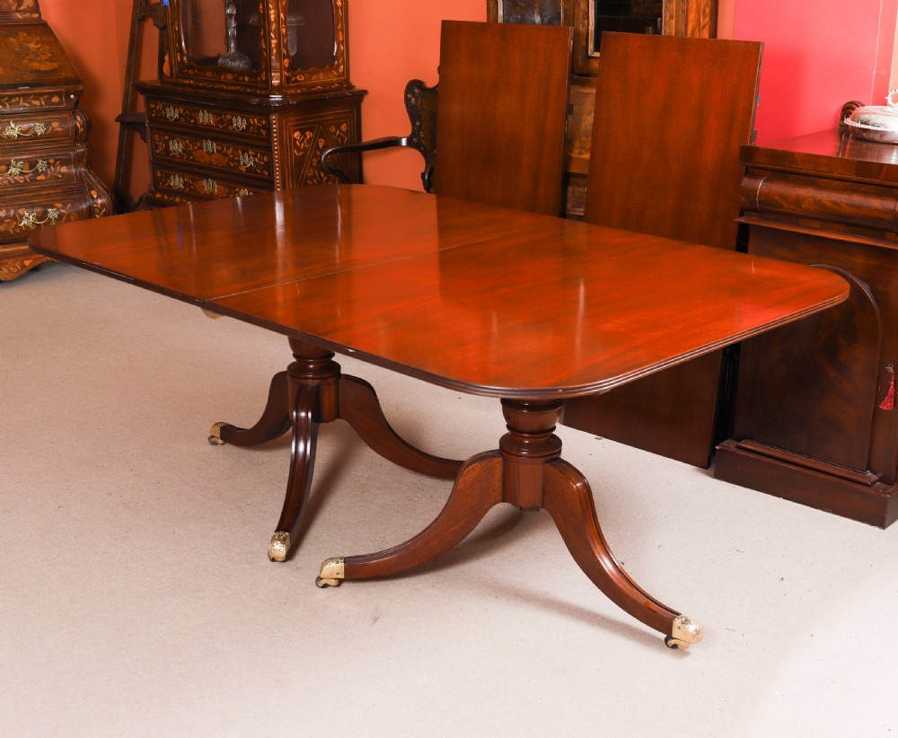 A long polished mahogany triple pillar dining table featuring splayed tripod legs fitted with brass castors. View IV