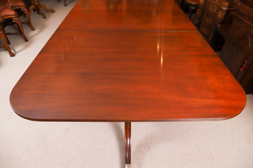 A long polished mahogany triple pillar dining table featuring splayed tripod legs fitted with brass castors. View V