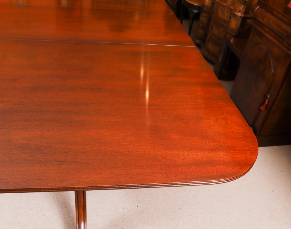 A long polished mahogany triple pillar dining table featuring splayed tripod legs fitted with brass castors. View VII