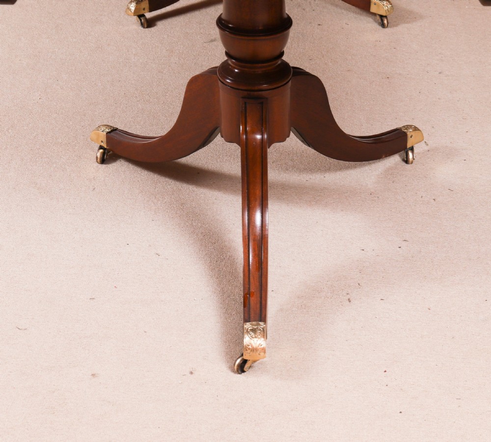 A long polished mahogany triple pillar dining table featuring splayed tripod legs fitted with brass castors. View VIII