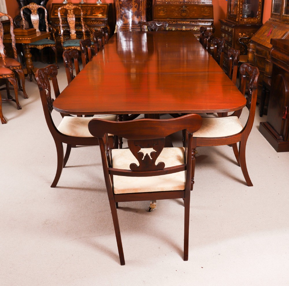 A long polished mahogany triple pillar dining table featuring splayed tripod legs fitted with brass castors. View IX