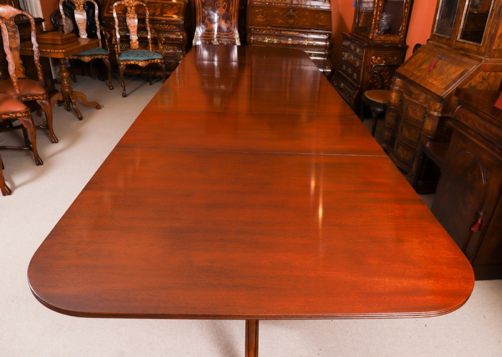 A long polished mahogany triple pillar dining table featuring splayed tripod legs fitted with brass castors. View XI