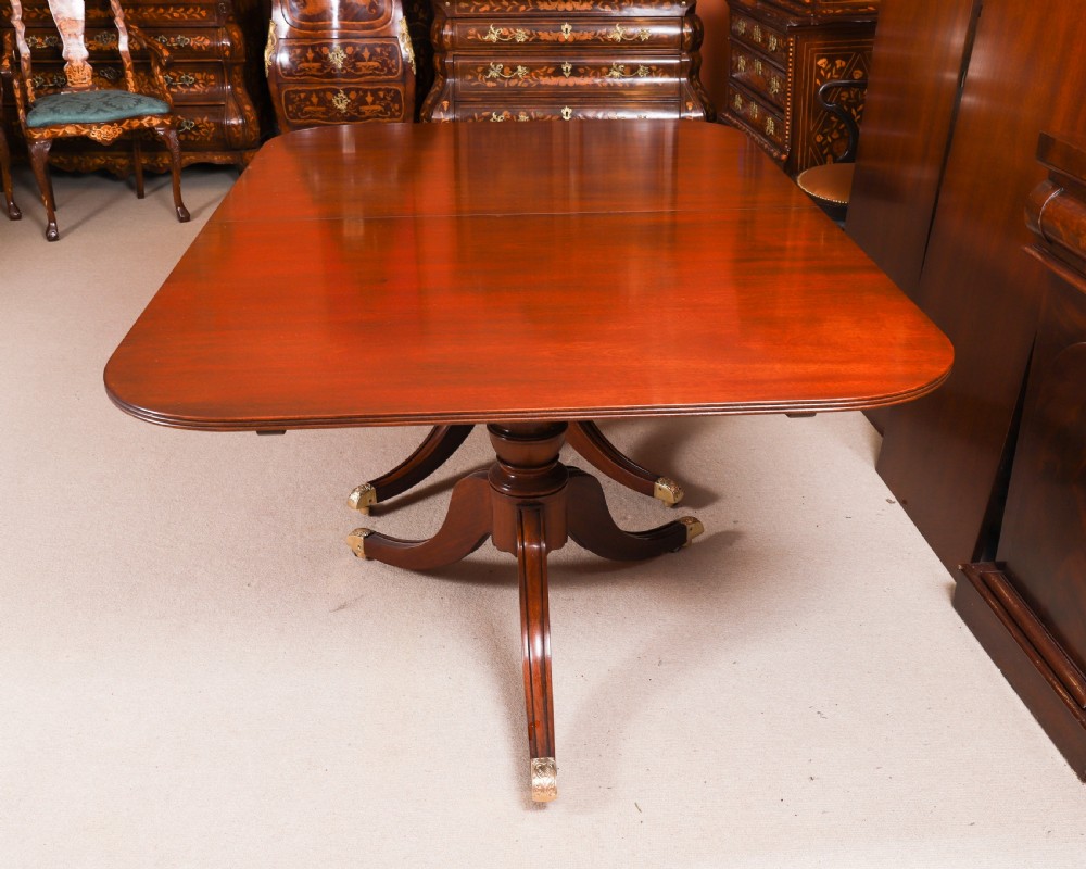 A long polished mahogany triple pillar dining table featuring splayed tripod legs fitted with brass castors. View XII