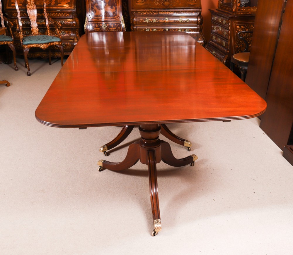 A long polished mahogany triple pillar dining table featuring splayed tripod legs fitted with brass castors. View XIII