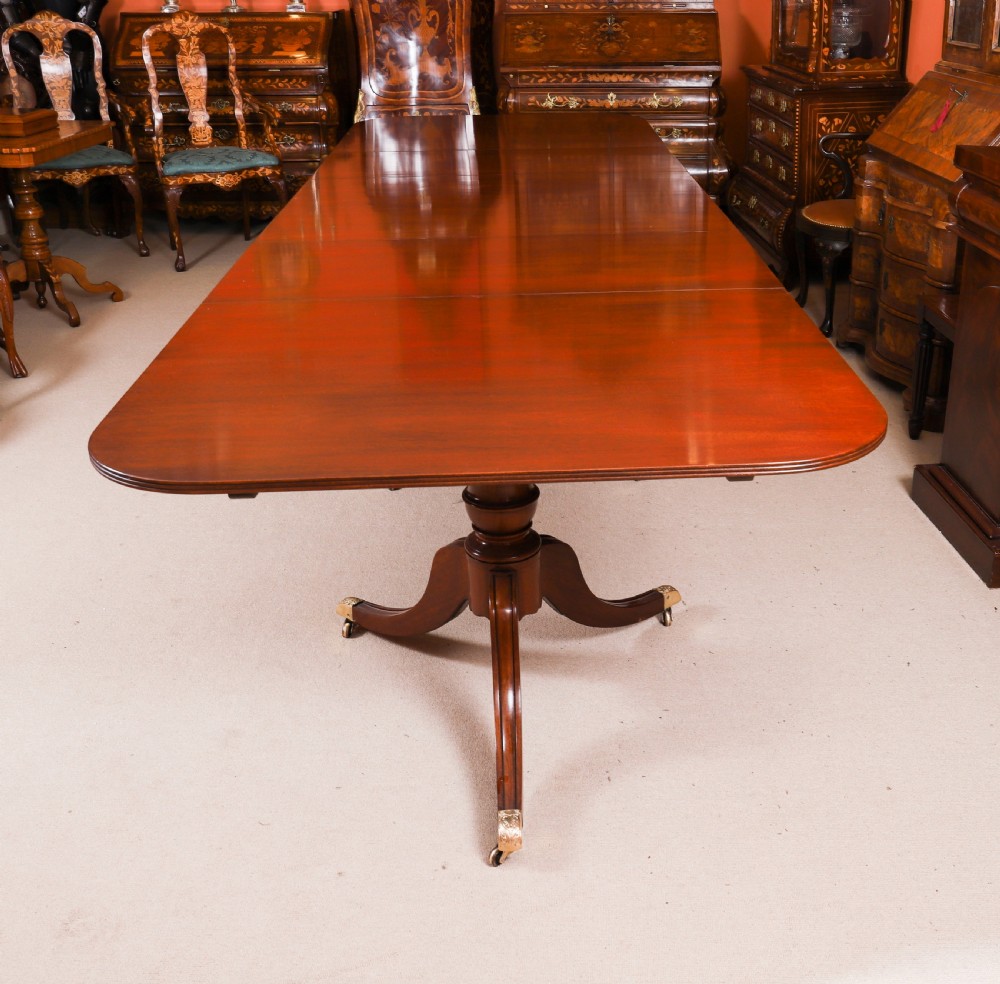 A long polished mahogany triple pillar dining table featuring splayed tripod legs fitted with brass castors. View XIV