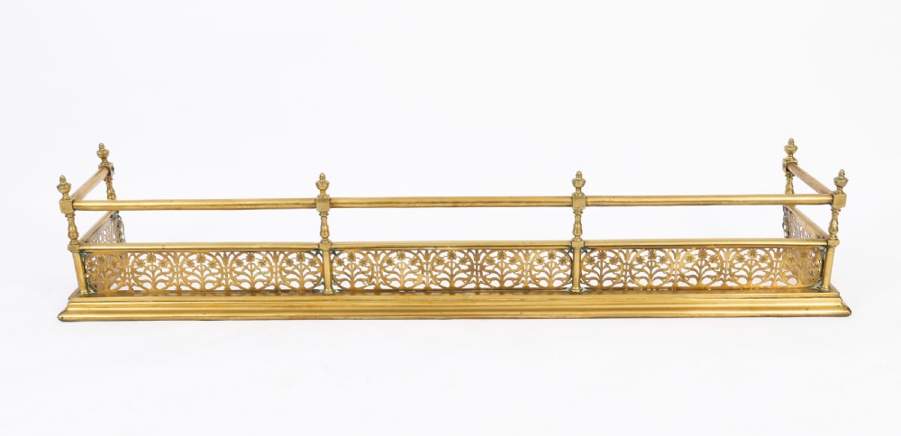 A 19th-century Victorian polished brass fireplace fender featuring a low pierced floral base band topped with a tubular rail supported by finial uprights. View II