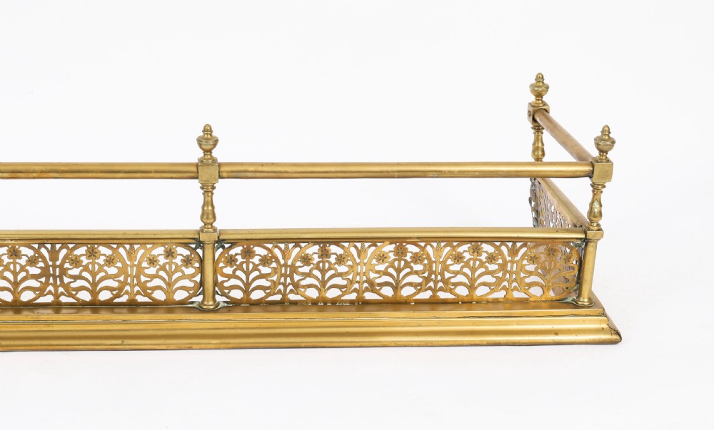 A 19th-century Victorian polished brass fireplace fender featuring a low pierced floral base band topped with a tubular rail supported by finial uprights. View III