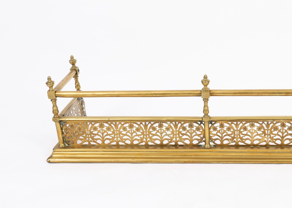 A 19th-century Victorian polished brass fireplace fender featuring a low pierced floral base band topped with a tubular rail supported by finial uprights. View IV