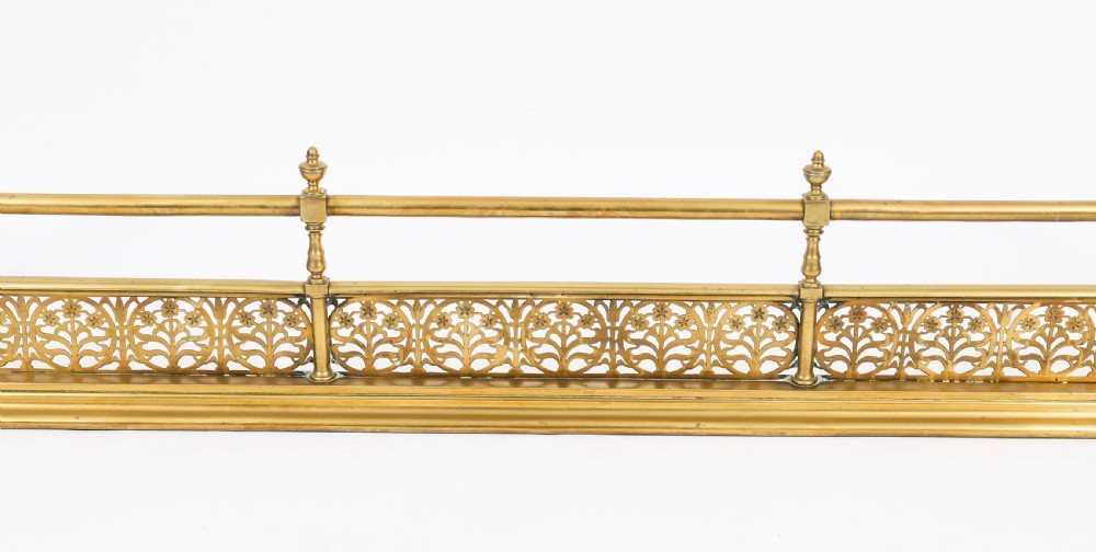 A 19th-century Victorian polished brass fireplace fender featuring a low pierced floral base band topped with a tubular rail supported by finial uprights. View VII