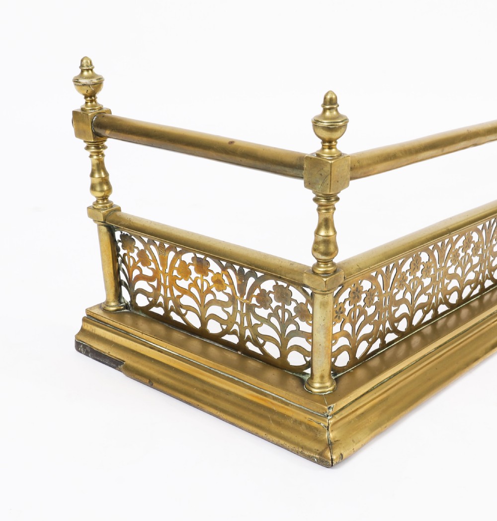 A 19th-century Victorian polished brass fireplace fender featuring a low pierced floral base band topped with a tubular rail supported by finial uprights. View VIII