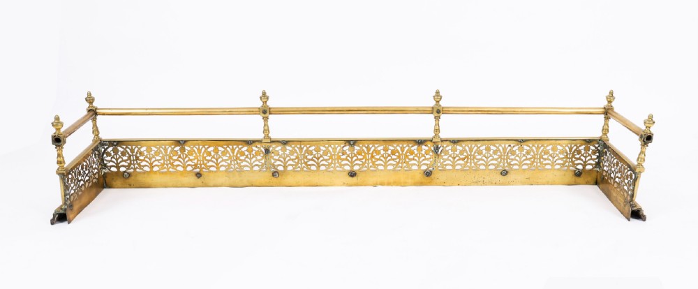 A 19th-century Victorian polished brass fireplace fender featuring a low pierced floral base band topped with a tubular rail supported by finial uprights. View IX