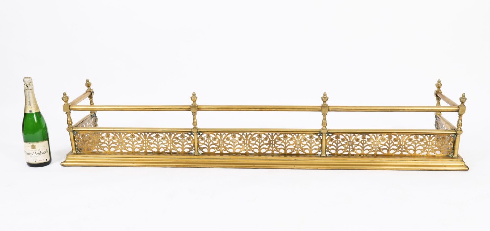 A 19th-century Victorian polished brass fireplace fender featuring a low pierced floral base band topped with a tubular rail supported by finial uprights. View X