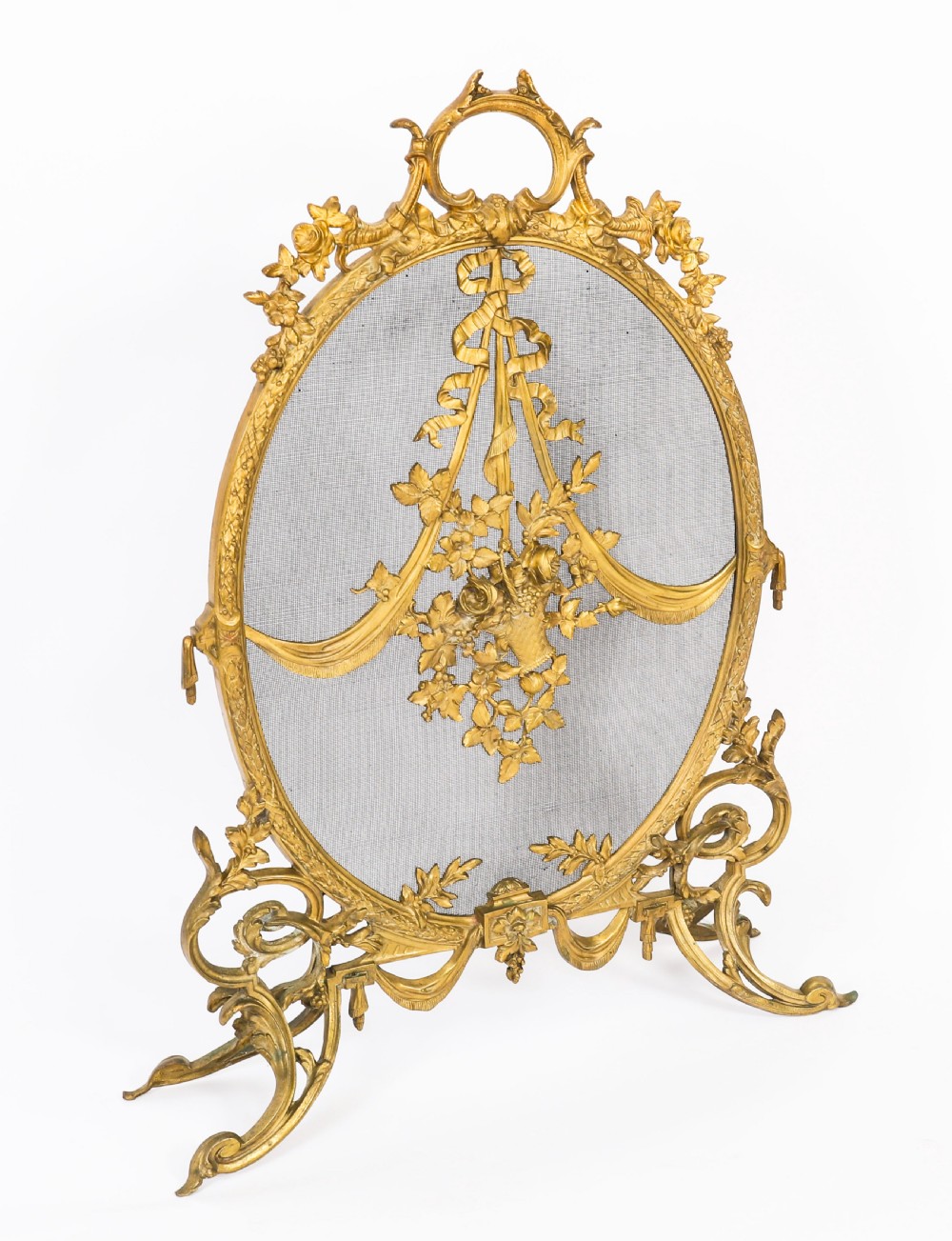 A 19th-century French Rococo Revival brass fire screen with an oval wire mesh insert, ornate bow knot and floral motif, resting on scroll feet.