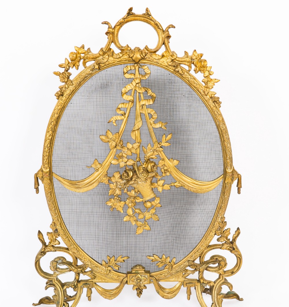 A 19th-century French Rococo Revival brass fire screen with an oval wire mesh insert, ornate bow knot and floral motif, resting on scroll feet. View VII