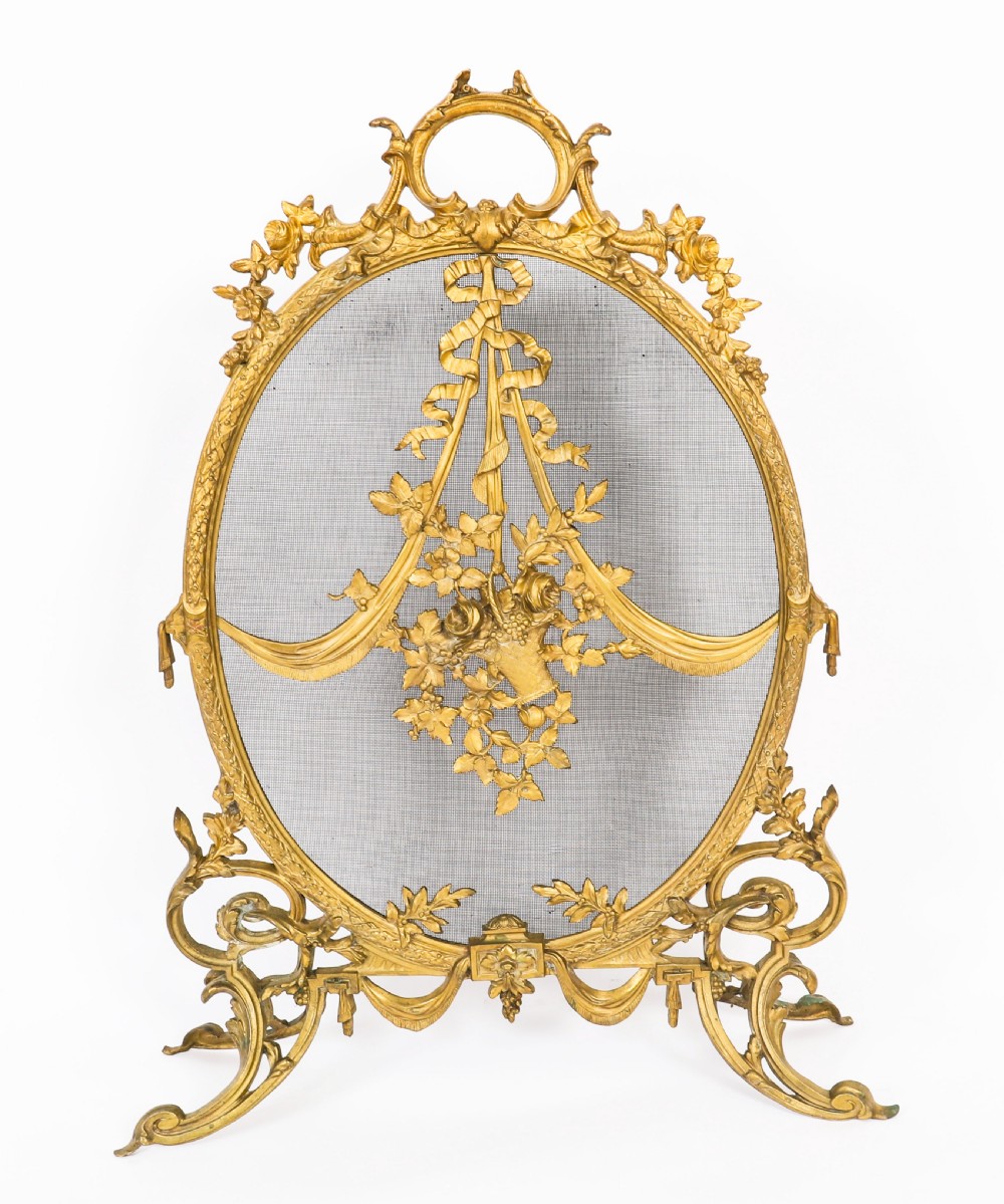 A 19th-century French Rococo Revival brass fire screen with an oval wire mesh insert, ornate bow knot and floral motif, resting on scroll feet. View XI