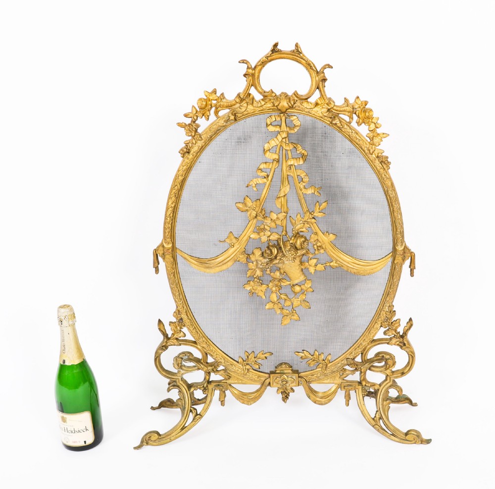 A 19th-century French Rococo Revival brass fire screen with an oval wire mesh insert, ornate bow knot and floral motif, resting on scroll feet. View XII