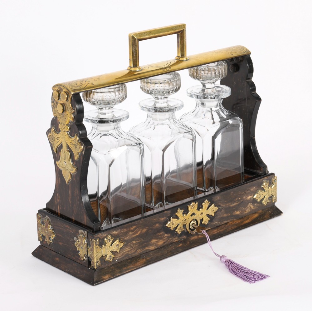 A Victorian coromandel wood tantalus with pierced brass corner mounts and top handle containing three cut crystal decanters with matching stoppers.