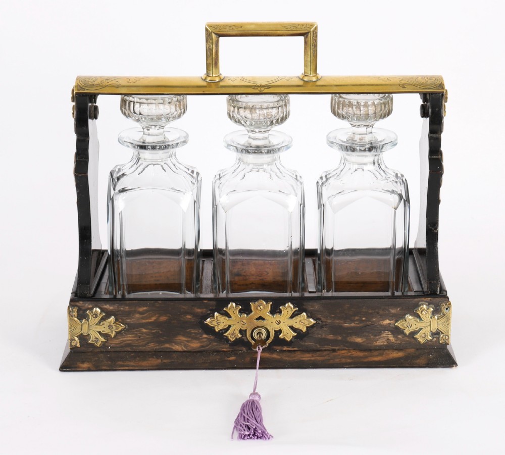 A Victorian coromandel wood tantalus with pierced brass corner mounts and top handle containing three cut crystal decanters with matching stoppers. View II