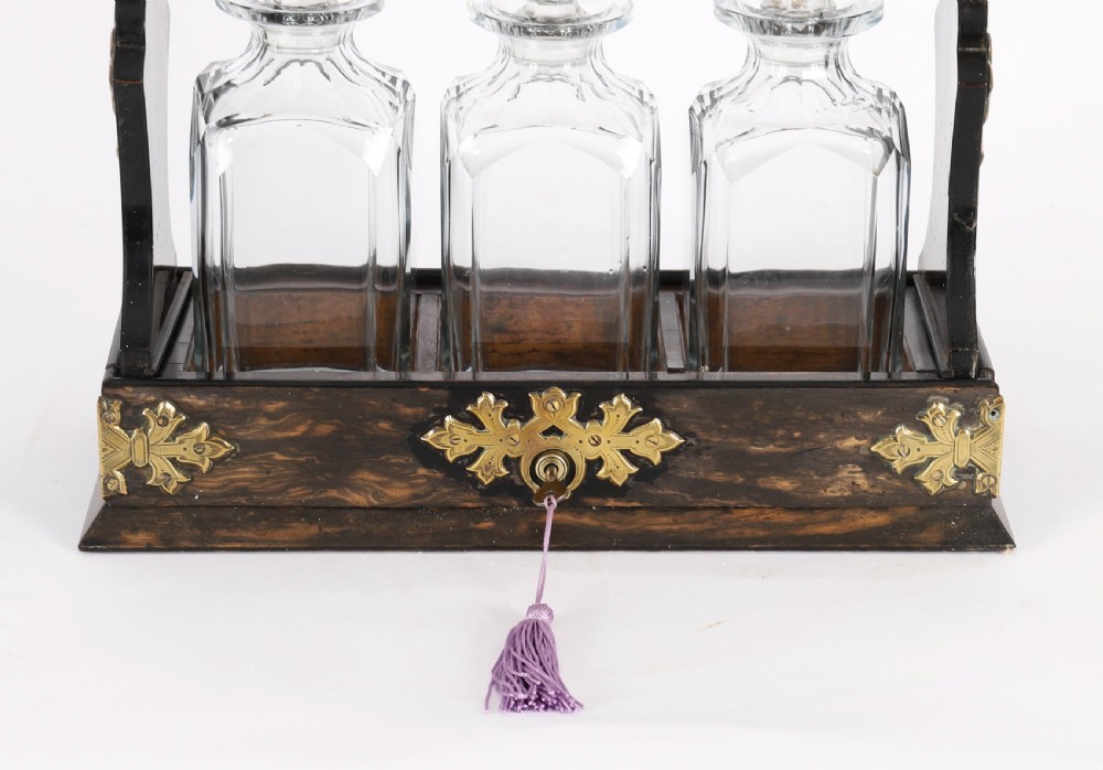 A Victorian coromandel wood tantalus with pierced brass corner mounts and top handle containing three cut crystal decanters with matching stoppers. View IV