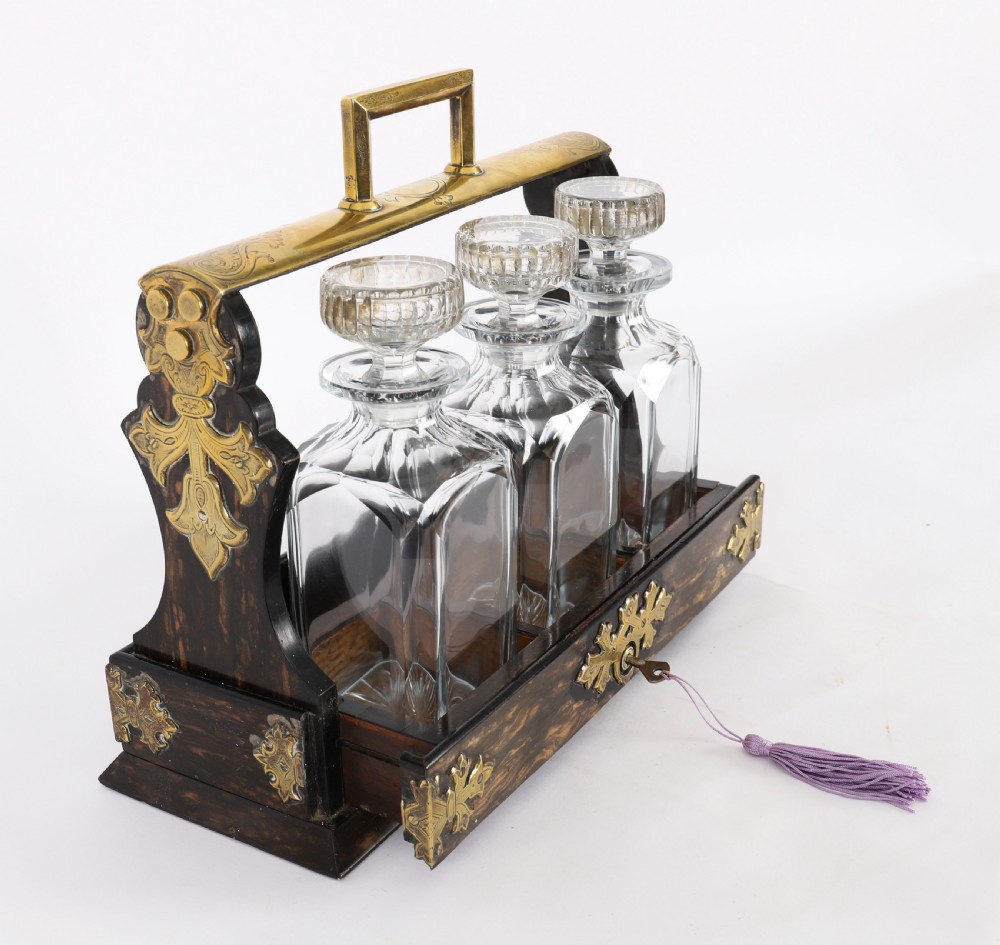 A Victorian coromandel wood tantalus with pierced brass corner mounts and top handle containing three cut crystal decanters with matching stoppers. View VI