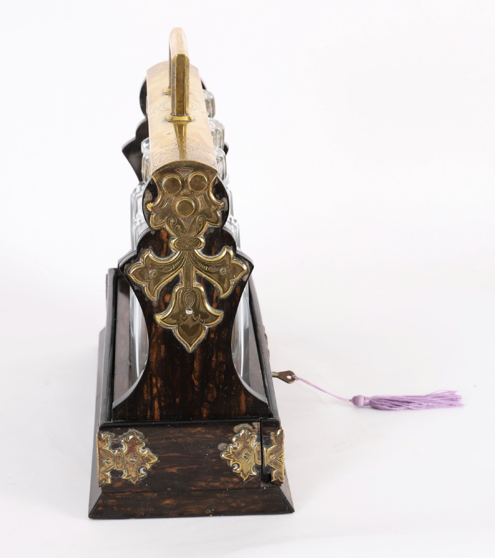 A Victorian coromandel wood tantalus with pierced brass corner mounts and top handle containing three cut crystal decanters with matching stoppers. View X