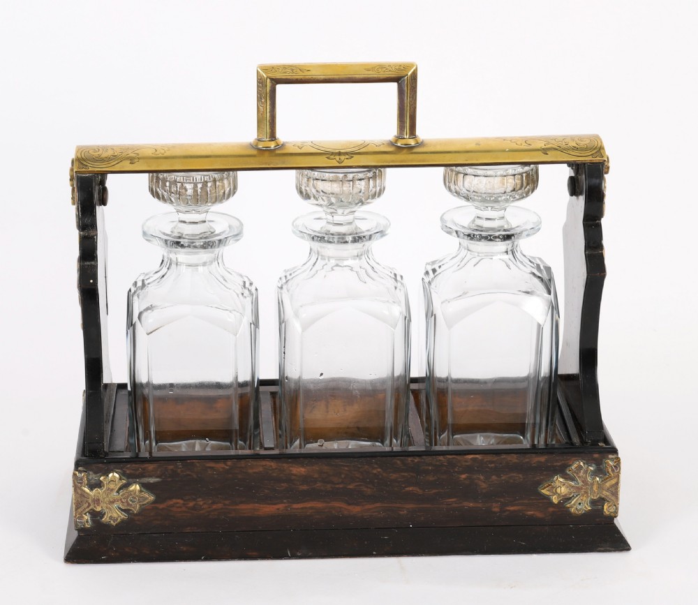 A Victorian coromandel wood tantalus with pierced brass corner mounts and top handle containing three cut crystal decanters with matching stoppers. View XV