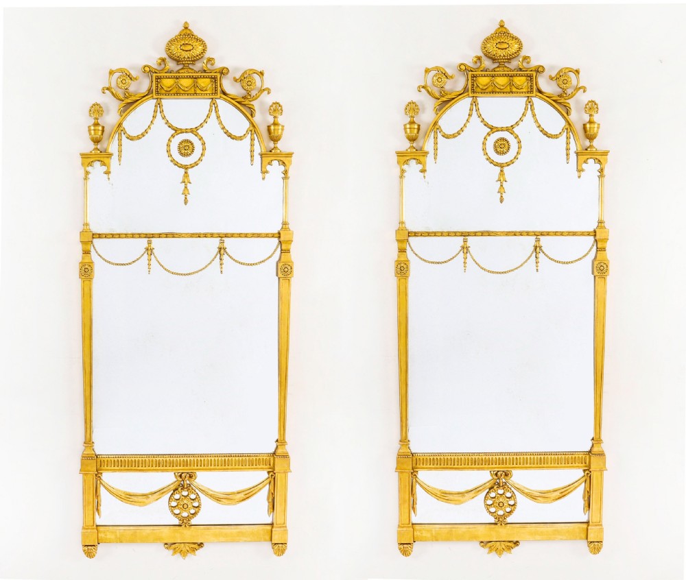 A matching pair of tall 19th-century Neoclassical giltwood pier mirrors decorated with urn crests, draped swags, and rosette motifs.