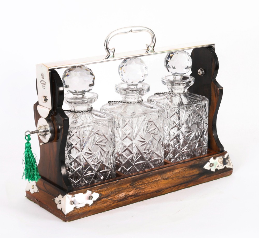 An Edwardian Betjemanns coromandel wood tantalus with hallmarked silver mounts holding three cut-crystal decanters.