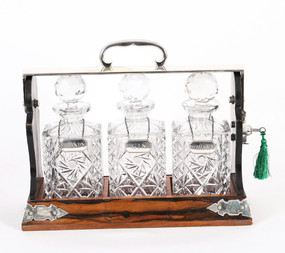 An Edwardian Betjemanns coromandel wood tantalus with hallmarked silver mounts holding three cut-crystal decanters. View II