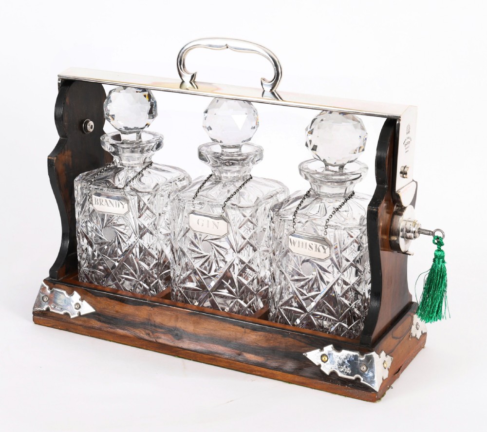 An Edwardian Betjemanns coromandel wood tantalus with hallmarked silver mounts holding three cut-crystal decanters. View IV