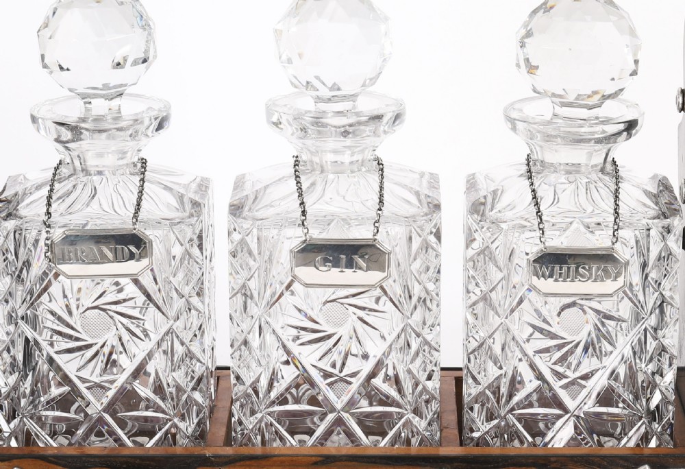 An Edwardian Betjemanns coromandel wood tantalus with hallmarked silver mounts holding three cut-crystal decanters. View V