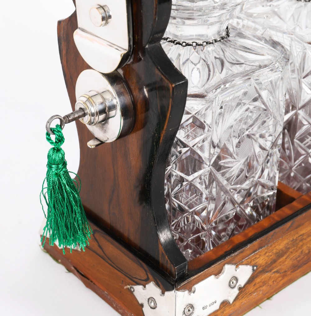 An Edwardian Betjemanns coromandel wood tantalus with hallmarked silver mounts holding three cut-crystal decanters. View IX