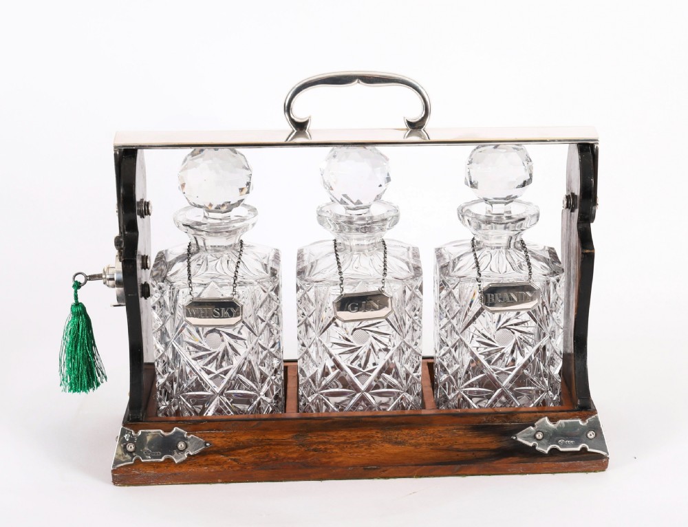 An Edwardian Betjemanns coromandel wood tantalus with hallmarked silver mounts holding three cut-crystal decanters. View XIV
