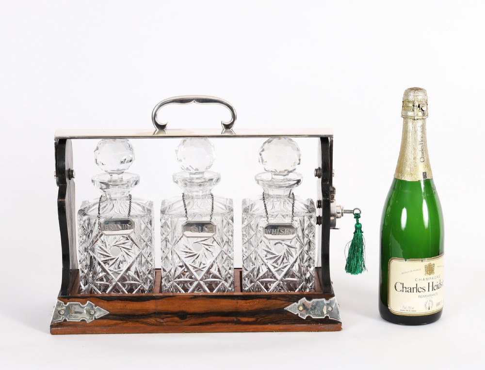 An Edwardian Betjemanns coromandel wood tantalus with hallmarked silver mounts holding three cut-crystal decanters. View XIX