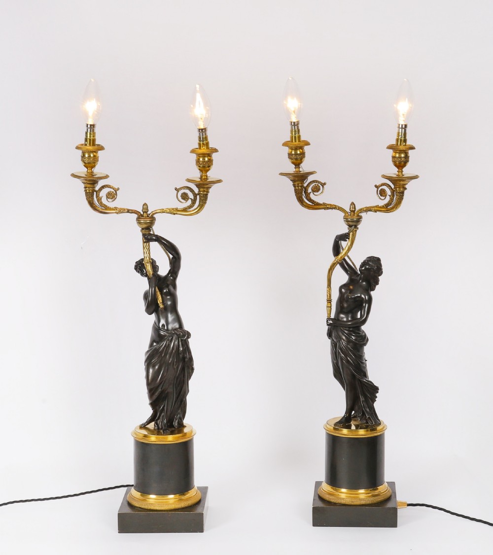 A pair of 19th-century French patinated bronze and gilt bronze two-light candelabra featuring classical draped female figures on cylindrical bases.