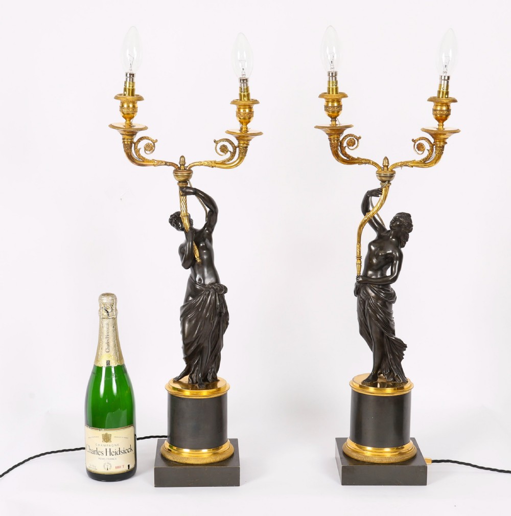 A pair of 19th-century French patinated bronze and gilt bronze two-light candelabra featuring classical draped female figures on cylindrical bases. View XIX