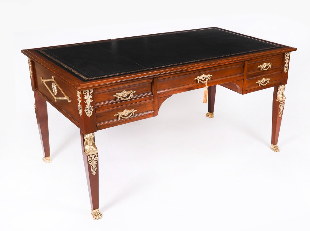 A nineteenth-century French Empire style mahogany bureau plat featuring gilt bronze ormolu mounts, tapered legs, five drawers, and a black leather writing surface.