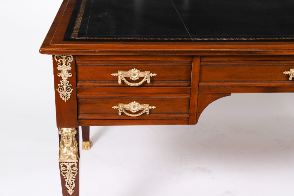 A nineteenth-century French Empire style mahogany bureau plat featuring gilt bronze ormolu mounts, tapered legs, five drawers, and a black leather writing surface. View IV