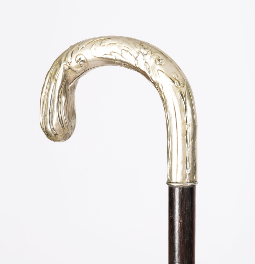 A 19th-century French Art Nouveau walking cane featuring a silver-plated crook handle decorated with foliate reliefs attached to a dark wooden shaft. View IV