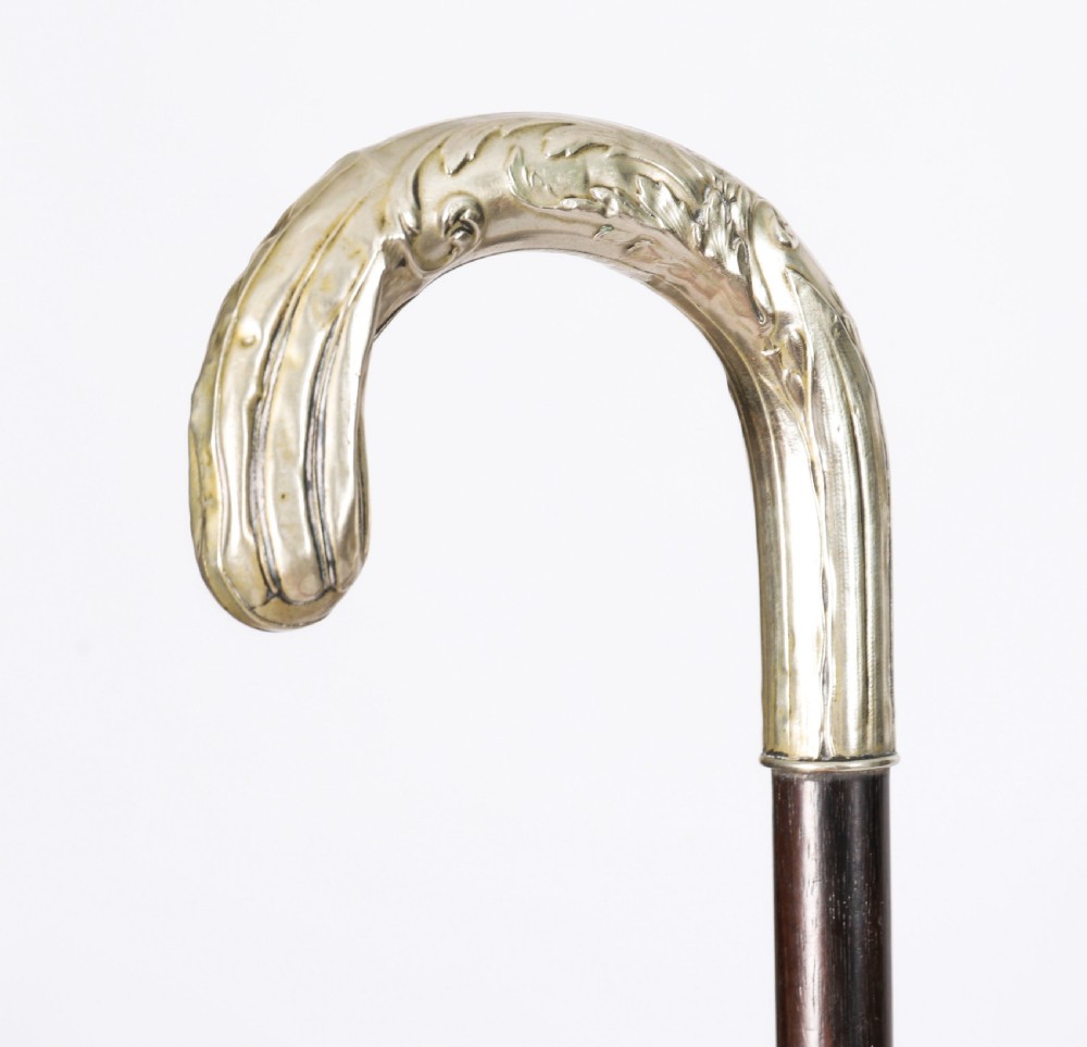 A 19th-century French Art Nouveau walking cane featuring a silver-plated crook handle decorated with foliate reliefs attached to a dark wooden shaft. View V