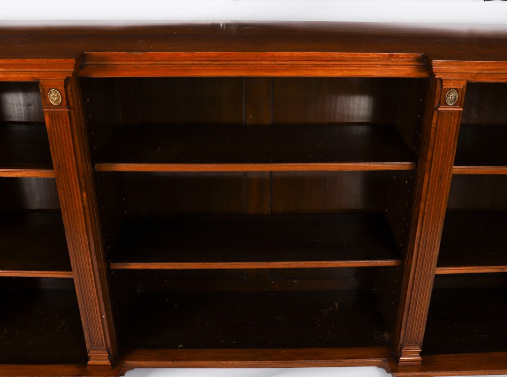 A wide Victorian open bookcase crafted in dark polished walnut with three bays of adjustable shelves, fluted pilasters adorned with circular ormolu mounts, and short turned feet. View VIII