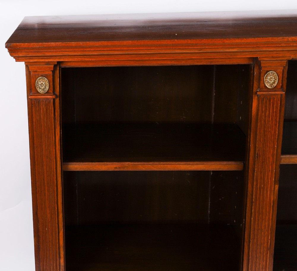 A wide Victorian open bookcase crafted in dark polished walnut with three bays of adjustable shelves, fluted pilasters adorned with circular ormolu mounts, and short turned feet. View X