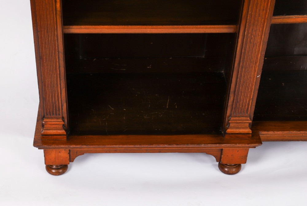 A wide Victorian open bookcase crafted in dark polished walnut with three bays of adjustable shelves, fluted pilasters adorned with circular ormolu mounts, and short turned feet. View XV