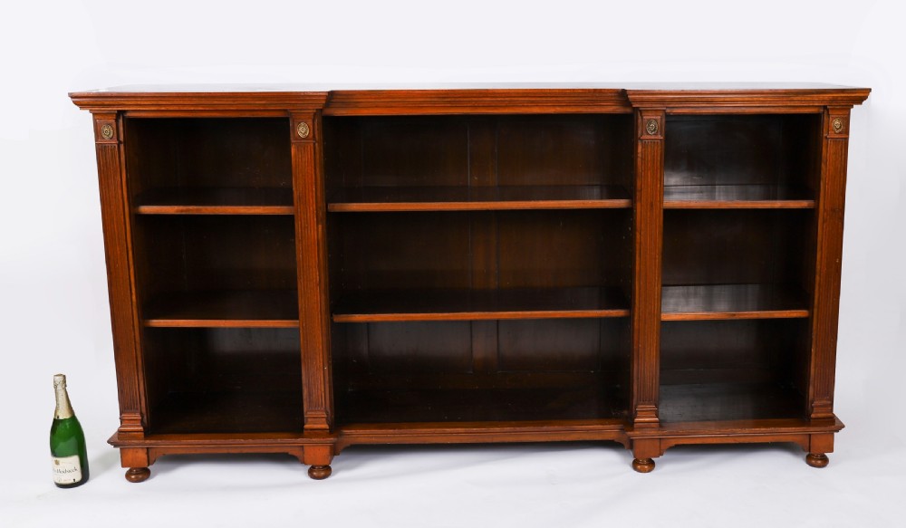 A wide Victorian open bookcase crafted in dark polished walnut with three bays of adjustable shelves, fluted pilasters adorned with circular ormolu mounts, and short turned feet. View XVI