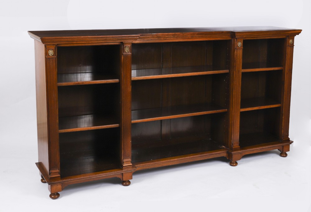 A wide Victorian open bookcase crafted in dark polished walnut with three bays of adjustable shelves, fluted pilasters adorned with circular ormolu mounts, and short turned feet.