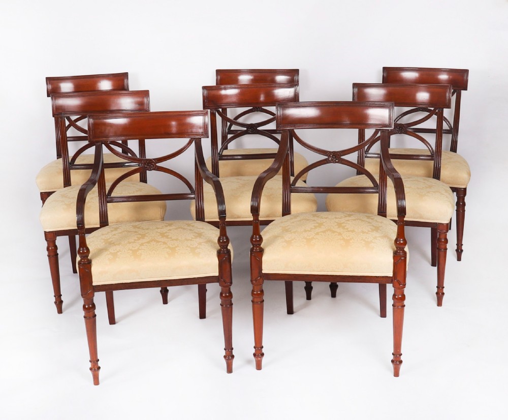 A set of eight Regency mahogany dining chairs with carved X-frame splats, reeded turned front legs, and light damask upholstered seats.