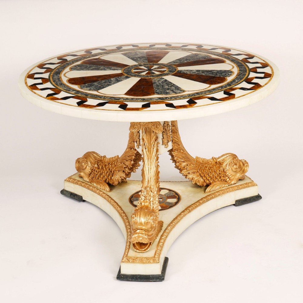 A circular centre table featuring an intricate geometric inlaid marble top supported by three carved gilt dolphin figures on a triform marble base. View II